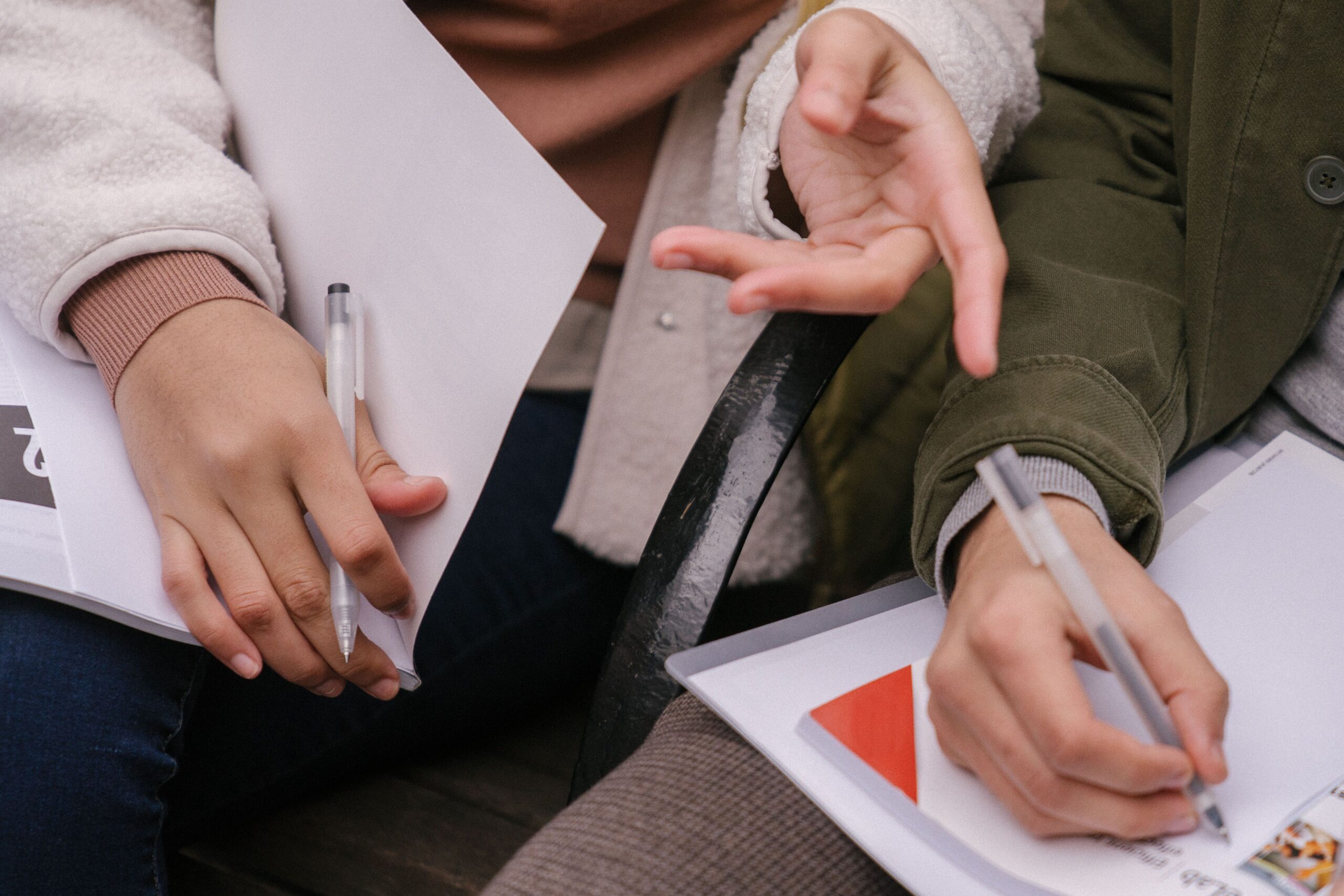 A photo of people's hands holding pens and writing.